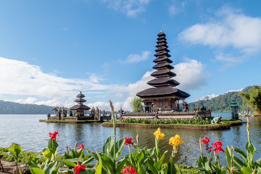 A lakeside temple framed by tropical flowers under a bright sky